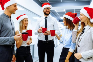 Noel Baba şapkalı başarılı genç işadamları bayramı kutluyor ve modern bir ofiste kırmızı bardaklardan bir içki içiyorlar. Mutlu yıllar ve mutlu Noeller..
