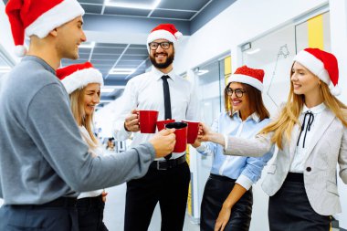 Noel Baba şapkalarıyla çalışan ekip, ofiste mola verirken, yeni yılı selamlar ve kırmızı bardaklardan bir içki içer.