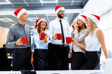 Noel Baba şapkalı genç iş adamları modern bir ofiste bayramı kutluyorlar. Bir grup genç iş adamı içki içip eğleniyor.