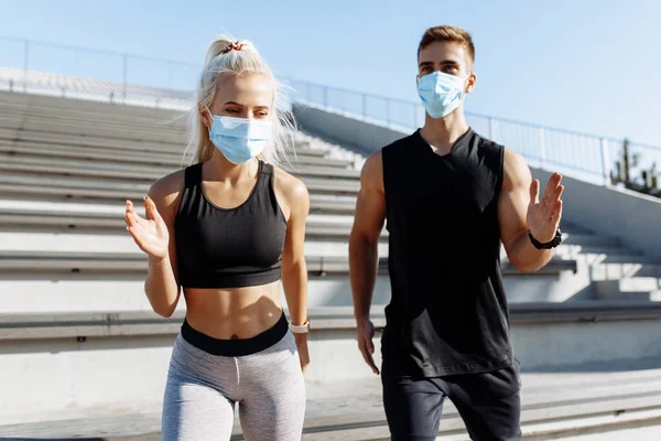 Young sports couple man and woman, in medical protective masks on their faces and in sportswear, running together along the street in the city, quarantine, coronavirus
