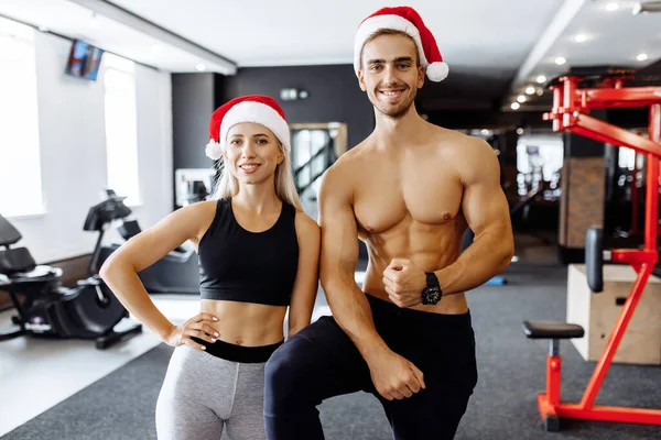 Mutlu spor çift, Noel Baba şapkalı spor giyim, spor salonundaki kaslarını göster, spor konseptini, yeni yılı