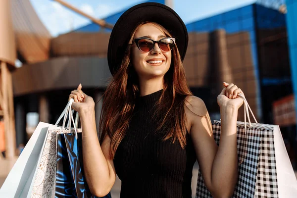 幸せな魅力的なエレガントな女の子は 黒のドレスと帽子で 暗いメガネを着用し ショッピングバッグを保持し 買い物を楽しむ ブラック フライデーショッピング — ストック写真