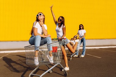 Genç, gülümseyen kadın arkadaşların alışveriş merkezinin yakınındaki alışveriş arabasıyla eğlendikleri görüntüler.