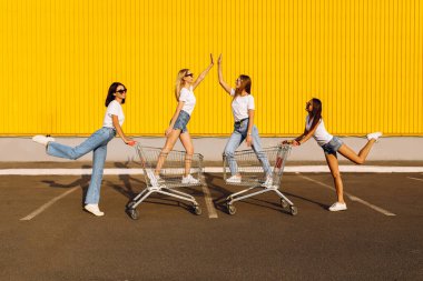 Grup genç arkadaşları, eğlenen genç kadınlar yazın güneşli bir günde alışveriş merkezinin yakınındaki arabalara biniyorlar.