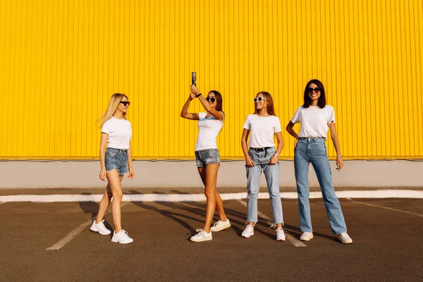 Group of excited young friends in sunglasses having fun and jumping throwing confetti outdoors on summer