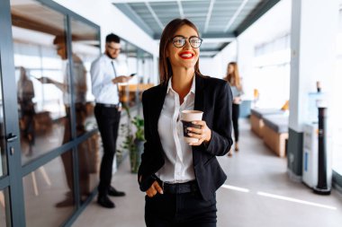 İş çekici genç bayan koridorda yürürken ofiste kahve içiyor.