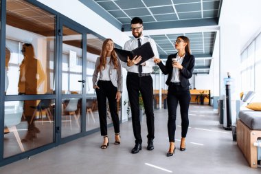 Ofis koridorunda yürürken konuşan ve belgelere bakan genç iş adamlarından oluşan bir ekip.