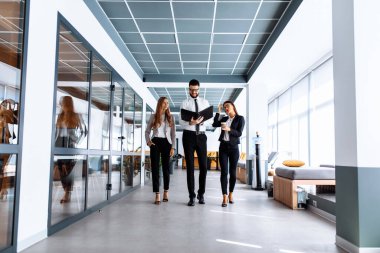 Ofis koridorunda yürürken konuşan ve belgelere bakan genç iş adamlarından oluşan bir ekip.