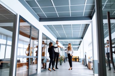 Çekici iş adamlarından oluşan bir grup modern bir ofiste ayakta ve iletişim halindeler.