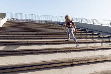 Spor giyim kuşamında, şehir merdivenlerinde spor yaparken koşan güzel ve genç bir bayan.
