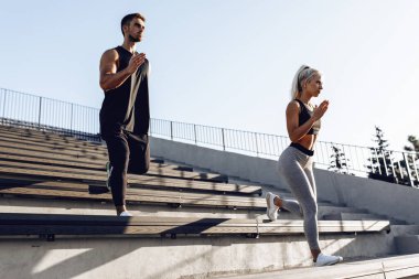 Merdivenlerde çalışıyoruz. Spor giyimli genç bir çift merdivenlerde, açık havada, sporda, sağlıklı bir yaşam tarzında birlikte koşuyorlar.