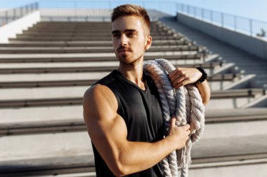 Sportif adam dışarıda spor yapıyor, kaslı adam iki dövüş ipi kullanıyor, spor, motivasyon.