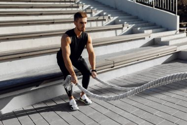 Sportif genç adam dışarıda spor yapıyor. Göğüs kaslı adam iki dövüş ipi, spor, motivasyon kullanıyor.
