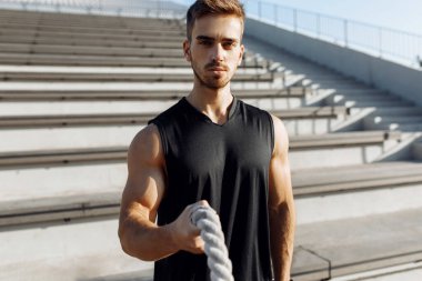 Sportif genç adam dışarıda spor yapıyor. Göğüs kaslı adam iki dövüş ipi, spor, motivasyon kullanıyor.