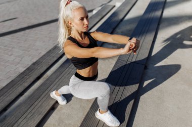 Şehir merdivenlerinde ısınma turlarında esneme hareketleri yapan spor giysili çekici genç bir kadın.