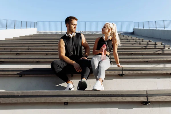 穿着运动服的年轻夫妇 休息一下喝水 坐在外面的楼梯上 健康的生活方式 — 图库照片