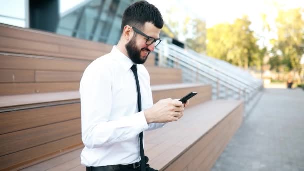 Χαρούμενη νεαρός επιχειρηματίας κομψά ντυμένος στο δρόμο της πόλης χρησιμοποιώντας το κινητό τηλέφωνο — Αρχείο Βίντεο