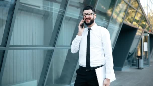 Joven empresario exitoso con barba hablando en el teléfono móvil al aire libre en la ciudad — Vídeos de Stock