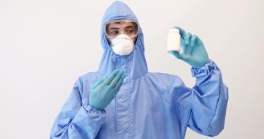 Koruyucu giysili, maskeli, gözlüklü ve eldivenli bir doktor elinde bir kutu hap tutuyordu. Sağlık konsepti, koronavirüs.