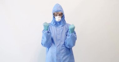 Covid-19 'la dövüşmek için koruyucu giysili bir doktor, gözlük, maske ve eldiven takıyor, beyaz bir arkaplanda zafer jesti gösteriyor.