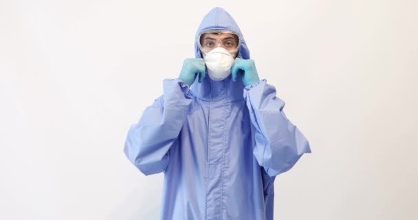 Medico maschio vestito con una tuta protettiva contro il coronavirus, indossando una maschera medica, occhiali e guanti, con le braccia incrociate su uno sfondo bianco. Quarantena, coronavirus — Video Stock
