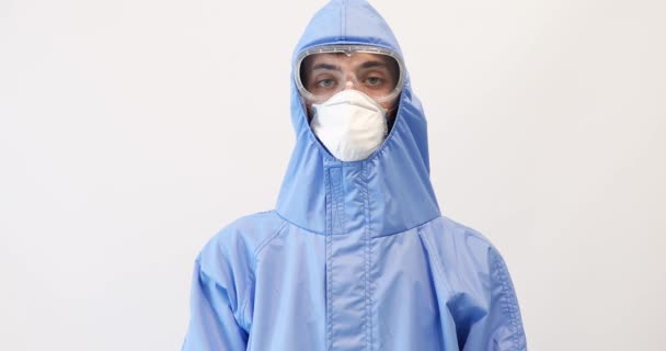 Man läkare klädd i en skyddsdräkt mot coronavirus, bär en medicinsk mask, glasögon och handskar, med armarna korsade på en vit bakgrund — Stockvideo