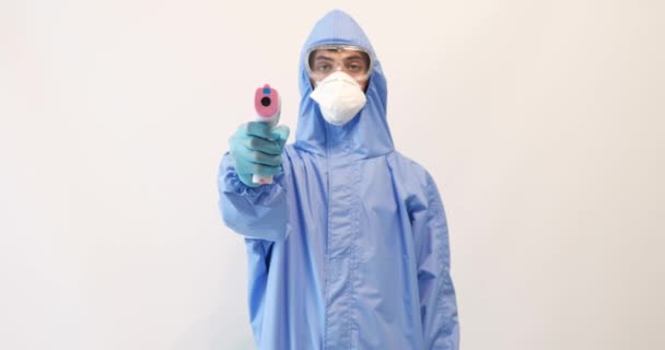 Męski lekarz noszący odzież ochronną, okulary, maskę i rękawice, z bezkontaktowym termometrem do pomiaru temperatury, na białym tle, epidemia koronawirusa — Wideo stockowe