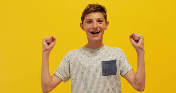 Feliz adolescente niño celebra la victoria sobre un fondo amarillo — Vídeos de Stock