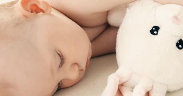 Niño pequeño en un pañal, durmiendo dulcemente en su cuna con un juguete de peluche — Vídeo de stock