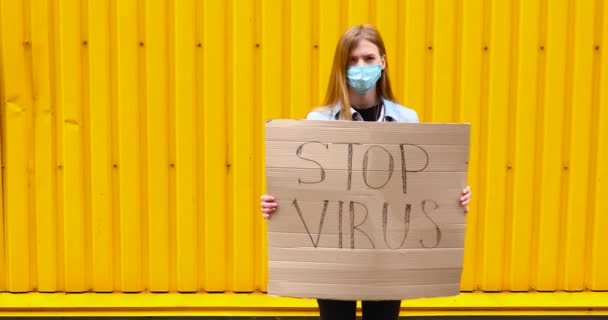 Vrouw in een medisch beschermend masker houdt een kartonnen bordje met de woorden — Stockvideo