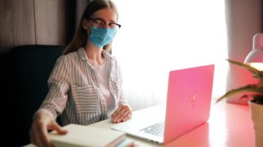  Yüzünde tıbbi koruyucu maske takmış genç bir öğrenci otururken ders çalışıyor. 