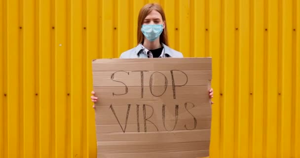 Woman in a medical protective mask holds a cardboard placard with the words — Stock Video