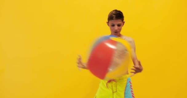 Щасливий збуджений хлопець стоїть з пляжним м'ячем ізольовано на жовтому — стокове відео