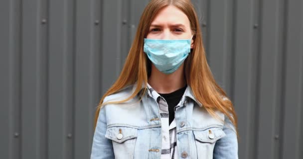 Vrouw in een medisch beschermend masker staande tegen een grijze muur — Stockvideo