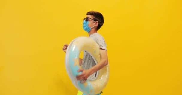 Adolescente cara anda por aí com um anel inflável e uma máscara protetora médica — Vídeo de Stock