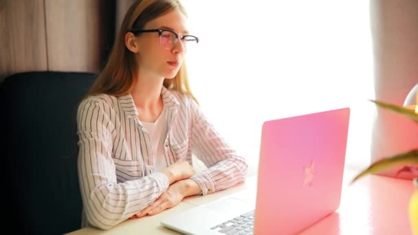 Joven mujer sonriente con gafas comunicándose con un cliente a través de un ordenador portátil — Vídeos de Stock