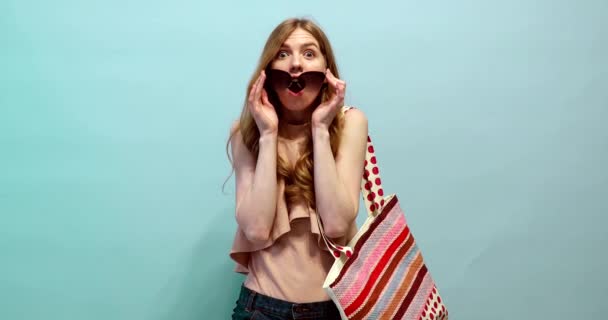 Geschokt en verrast meisje in een badpak en zonnebril, op een blauwe achtergrond — Stockvideo