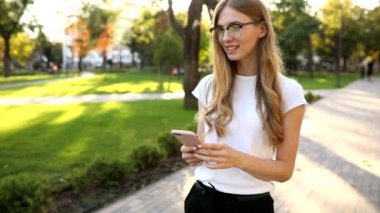 Sarışın, güzel bir kadın, cep telefonu kullanıyor, akıllı telefondan mesajlaşıyor, açık havada parkta.