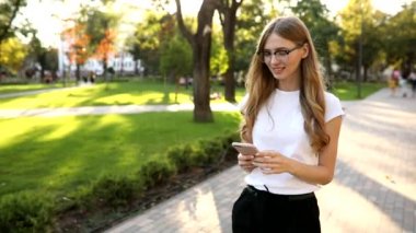 Sarışın, güzel bir kadın, cep telefonu kullanıyor, akıllı telefondan mesajlaşıyor, açık havada parkta.