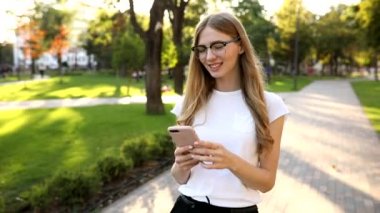 Sarışın, güzel bir kadın, cep telefonu kullanıyor, akıllı telefondan mesajlaşıyor, açık havada. 