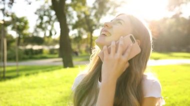 Genç, güzel, gülümseyen bir kız şehrin dışında cep telefonuyla konuşuyor.