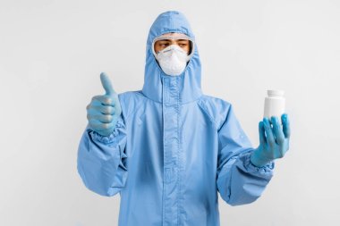 Koruyucu kıyafetli, maskeli, gözlüklü ve eldivenli bir doktor elinde bir kutu hap tutuyordu. Sağlık konsepti, koronavirüs, COVID-19