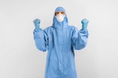 Coronavirus 'la savaşmak için koruyucu giysili bir doktor gözlük, maske ve eldivenlerle beyaz bir arkaplanda zafer jesti gösteriyor.