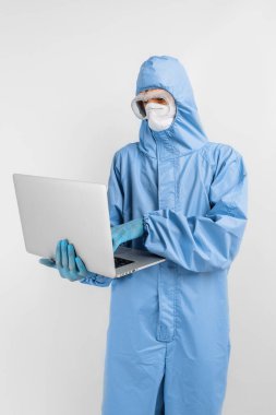 Koruyucu tıbbi giysi, maske, gözlük ve eldiven giyen erkek doktor, izole edilmiş beyaz bir arka plan, sağlık sigortası, hastalık önleme üzerinde dizüstü bilgisayar kullanarak çalışır.