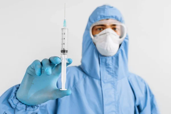 Male doctor in a protective medical suit, mask, glasses and gloves, holds a syringe with a vaccine against coronavirus, the concept of medical care, coronavirus