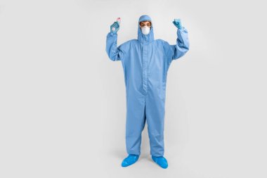 Covid-19 'la dövüşmek için koruyucu giysili bir doktor, gözlük, maske ve eldiven takıyor, beyaz bir arkaplanda zafer jesti gösteriyor.