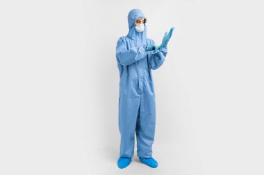 Koruyucu giysili, gözlüklü, maskeli ve eldivenli erkek doktor, beyaz arka plan, koronavirüs salgını konsepti