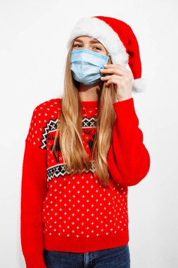 Çekici mutlu genç Noel Baba kadın Noel şapkası takıyor, tıbbi maske takıyor, Coperid-19 Coronavirus virüsünden korunuyor, beyaz arka planda, yeni yıl bayramını kutluyor.