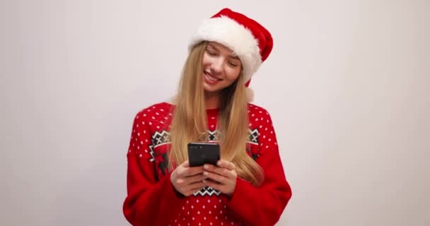 Młoda kobieta w Boże Narodzenie Santa Claus kapelusz, używa telefonu komórkowego, wpisując sms na białym tle — Wideo stockowe