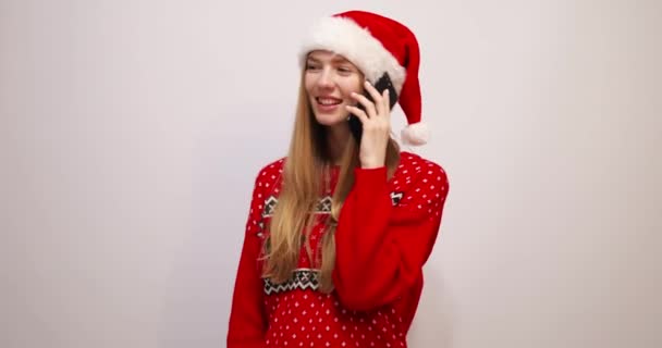 Sorrindo jovem mulher no Natal chapéu de Papai Noel falando no celular no fundo branco — Vídeo de Stock
